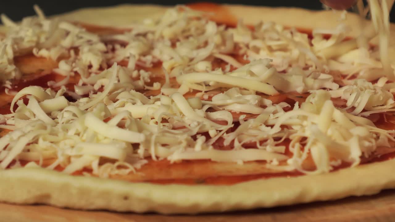 A close-up of grated cheese being placed on pizza dough with tomato sauce, highlighting the preparation process of homemade pizza.