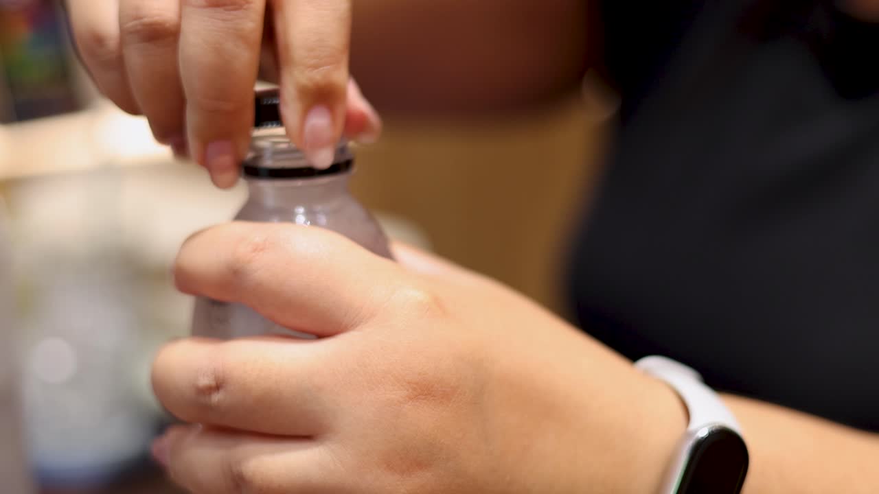Close-up of hands unscrewing a plastic water bottle cap indoors under warm, natural lighting