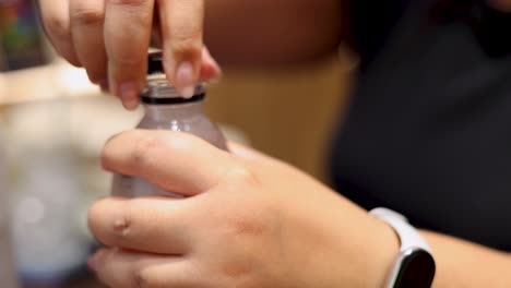 close-up of hands unscrewing a plastic water bottle cap indoors under warm, natural lighting