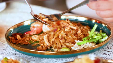 person eating shrimp pad thai with utensils