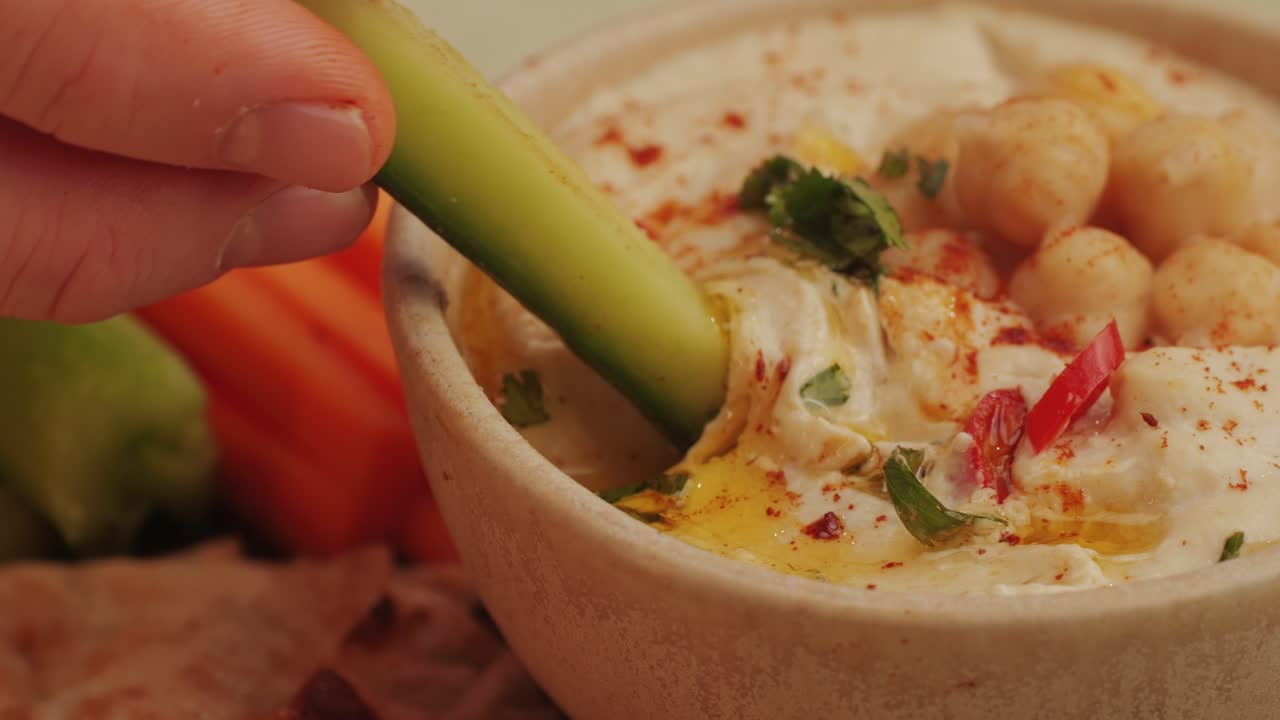 Dipping vegetable slice in hummus with spice and greens on top close-up. Hummus or fava, a healthy snack of legumes and chickpeas. Kosher healthy vegan food. Lean, vegetarian dish. High quality 4k footage