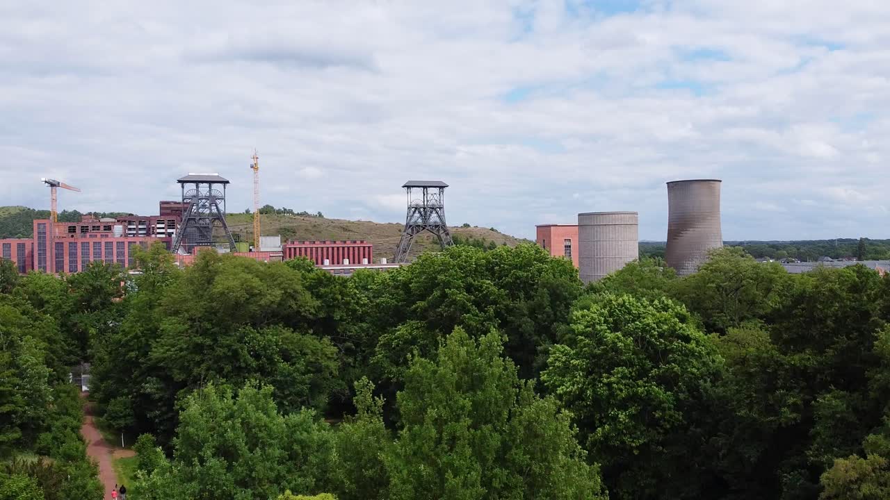Aerial above nature park with tall trees in front of historical mine buildings in Beringen, Belgium.