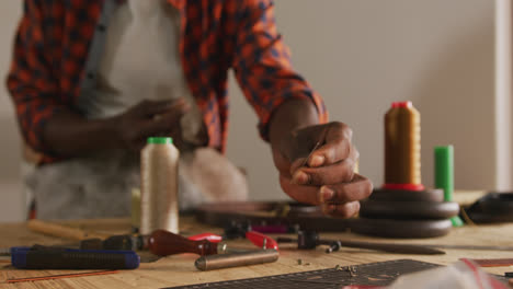 manos de un artesano afroamericano con un delantal y tomando herramientas en un taller de cuero