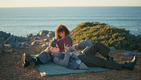 relaxed couple lying picnic blanket at marine nature. man reading book loud