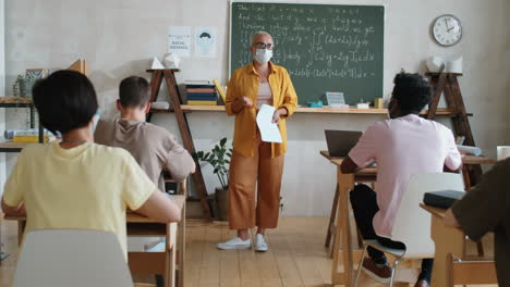 teacher in mask giving lesson to students in classroom