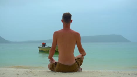 el hombre se sentó en la playa tropical, meditando, con hermosas vistas al mar