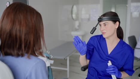 a happy and confident brunette girl. an ent doctor in a blue uniform explains to a girl patient a his ideas about the prevention of throat diseases. a brunette doctor girl in a blue uniform communicates with a patient in the ent office in a modern clinic