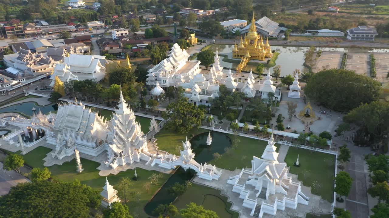 drone aéreo de wat rong khun el gran templo budista blanco y templo dorado con montañas y paisaje en chiang rai, tailandia