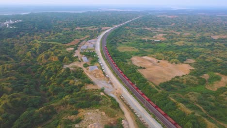 Toma-Aérea-De-Un-Tren-De-Carga-Que-Se-Mueve-A-Través-Del-Valle-Forestal-Semiárido-Del-Río-Chambal-En-La-India