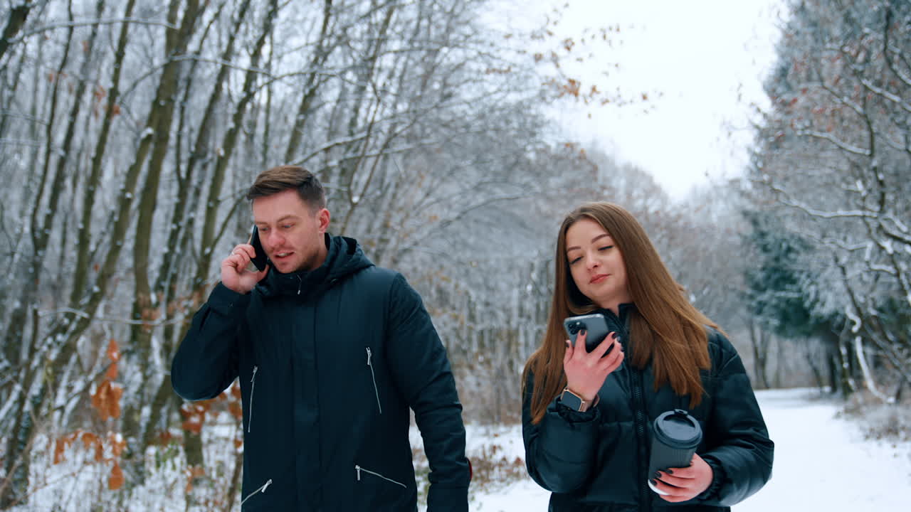 Caucasian people walk by the winter park speaking on their phones. Couple stops and cheers excitedly.