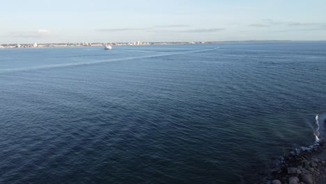 Aerial-view-of-the-Oresund-Strait-with-a-peaceful-Baltic-Sea-lapping-a-rocky-beach-without-people-in-Helsingor-on-a-sunny-day-and-a-ship-in-sight