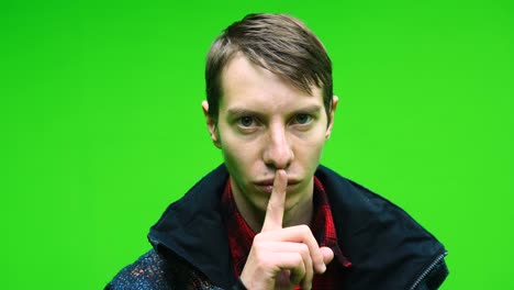 man in casual clothing is shushing on green screen background. mute point or stop with his gestures.