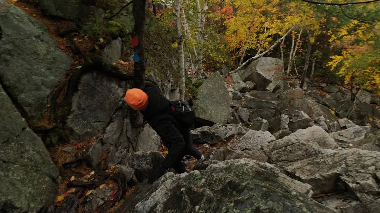 Young Man Climbs Huge Rocks in Fall Leaf Colors, Slow motion Handheld Pan