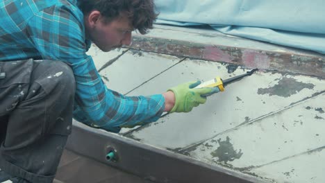 a carpenter applying sealant into seams of wooden boat hull planks