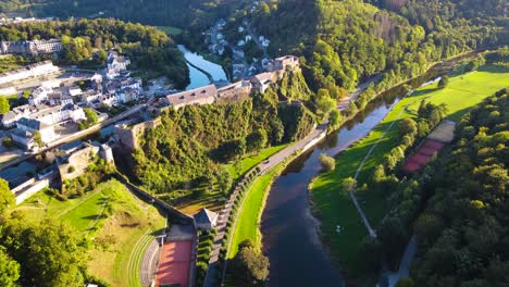 Toma-Aérea-Que-Se-Inclina-Hacia-Arriba-Desde-El-Río-Mosa-En-El-Campo-De-Bélgica-Para-Revelar-El-Castillo-De-Bouillon-En-Un-Terreno-Elevado