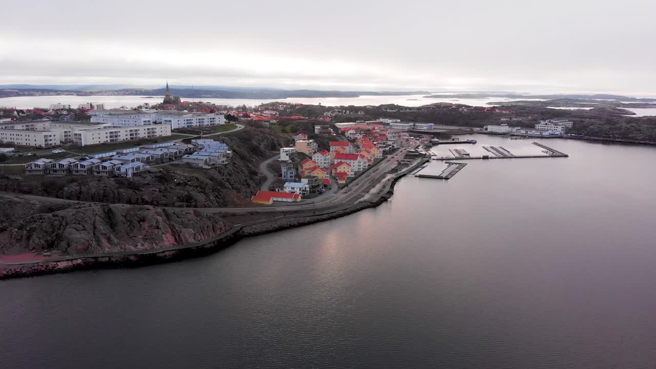 Flying over the beautiful red rooftops of by the waters of Lysekil, Sweden during a cloudy day - Aerial shot