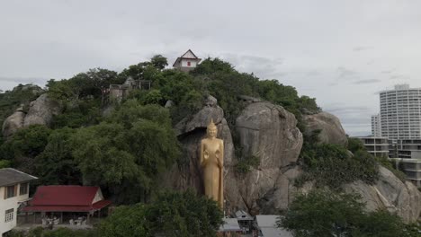 pullback from golden buddha statue standing on rock, near takiap beach, thailand