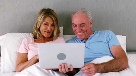 pareja sonriente acostada en la cama y usando una computadora portátil