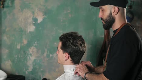 attractive young man sitting in a chair while bearded barber is preparing him for a haircut. stylish barber shot