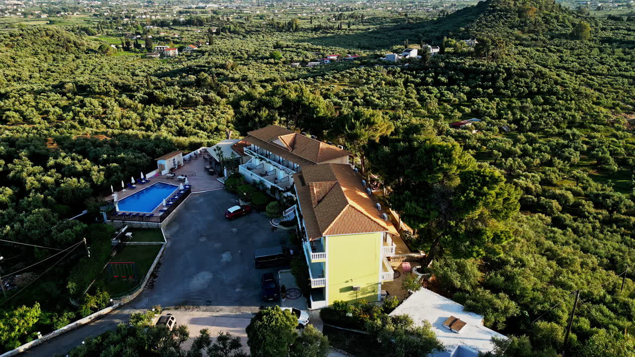 Luxury resort hotel with pool on small hill in Greek landscape, aerial orbit view
