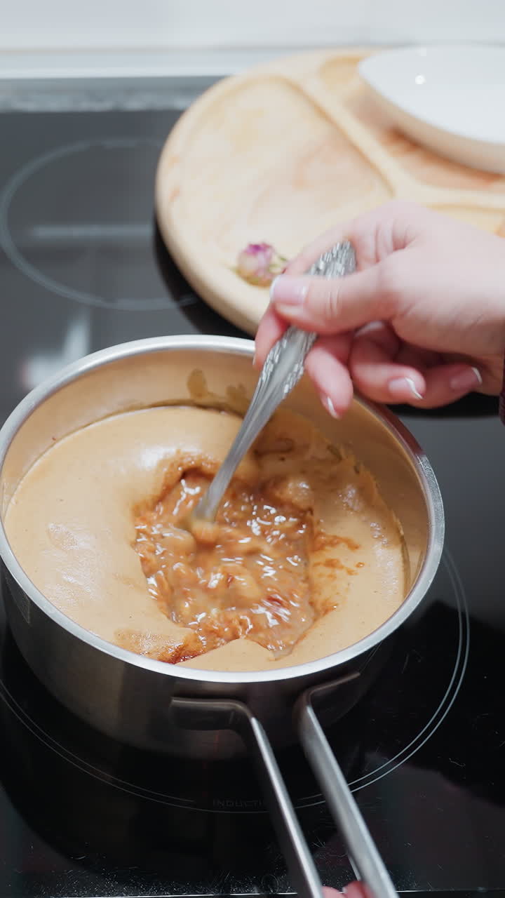 Close-up of chef stirring a pot of soup on an electric stove in a modern kitchen, the sleek countertop, wooden cutting board, and open cookbook enhance the cozy, organized cooking environment