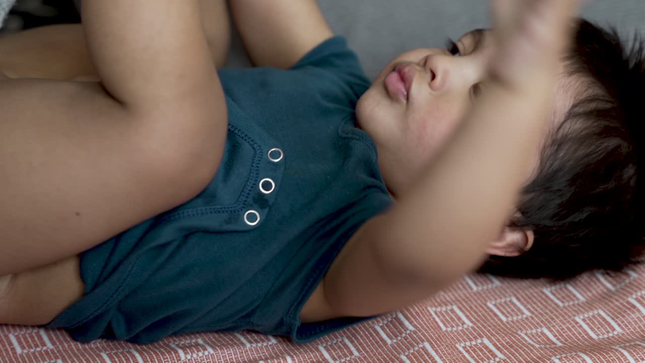 18 개월 된 아기의 기저귀 변경의 부드러운 순간은 느린 동작으로 포착되어 부드럽고 양육하는 아기 보살의 개념을 강조합니다.