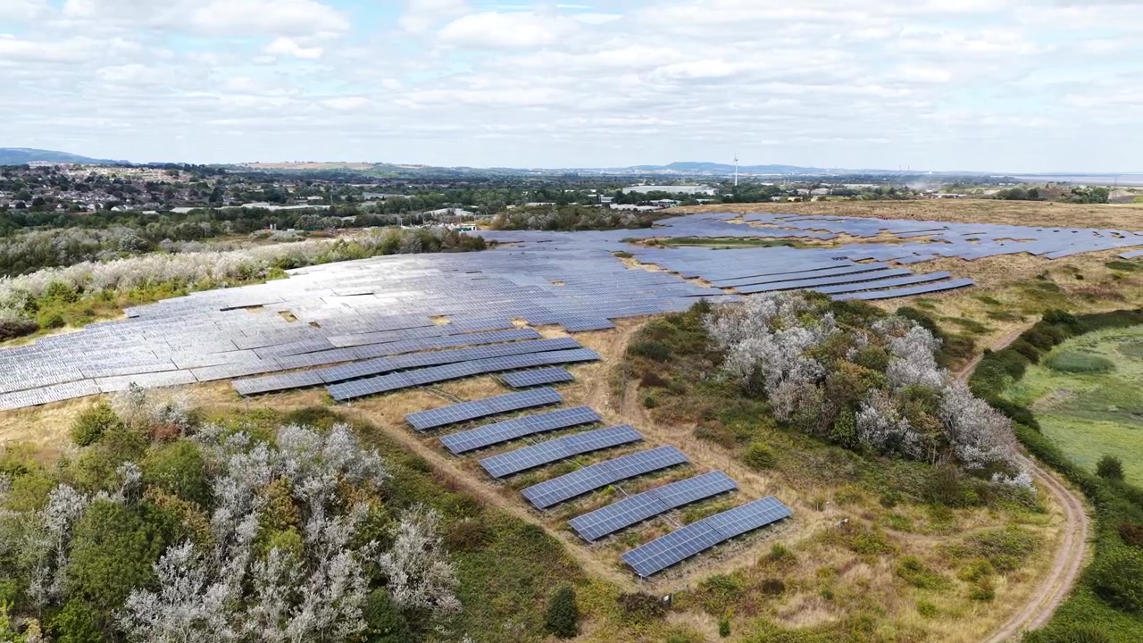 Droneoptagelse af en storstilet solcellepark nær Cardiff, Sydwales, med rækker af solcellepaneler, der genererer ren vedvarende elektricitet på en sommerdag