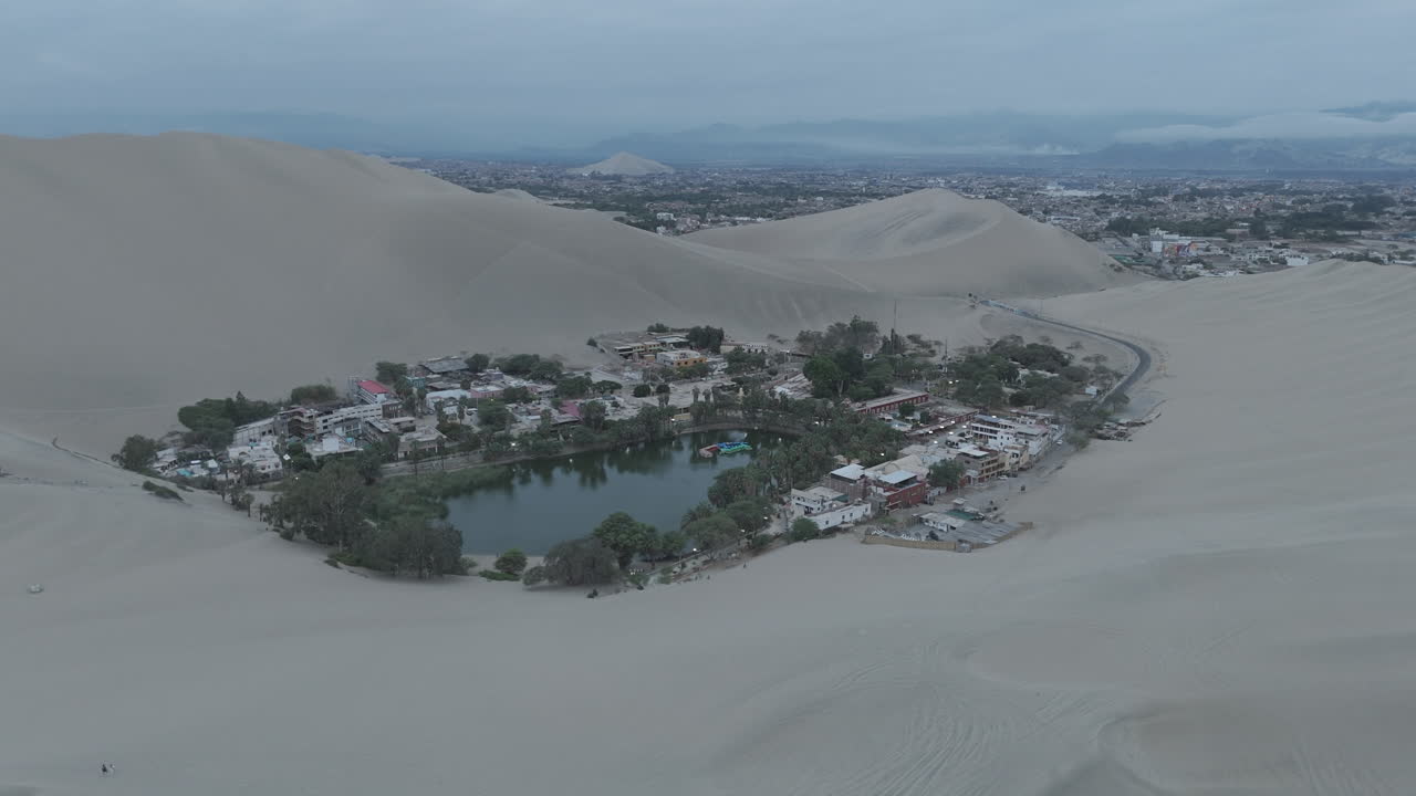 Drone shot revealing the city of Huacachina in Peru behind the dunes on a cloudy morning during the mist LOG
