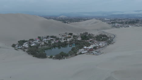 drone shot revealing the city of huacachina in peru behind the dunes on a cloudy morning during the mist log