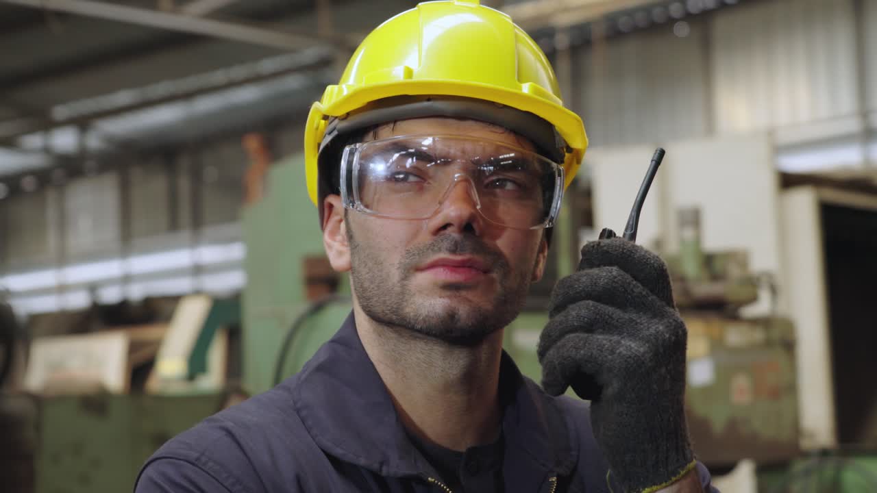 trabajador de una fábrica hablando por radio portátil mientras inspecciona piezas de maquinaria