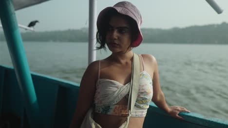 una mujer joven en un bikini blanco está de pie en un barco con un sombrero rosa en la india