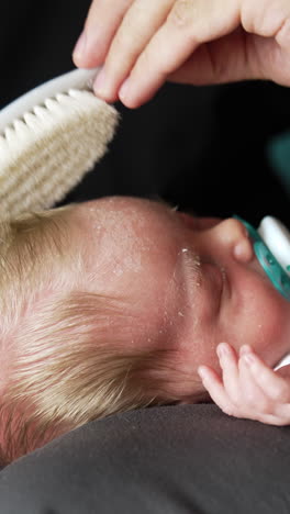 brushing the baby hair. adorable blonde newborn with quite long hair lies sleeping on dad's laps and father brushes his hair. close up. vertical video