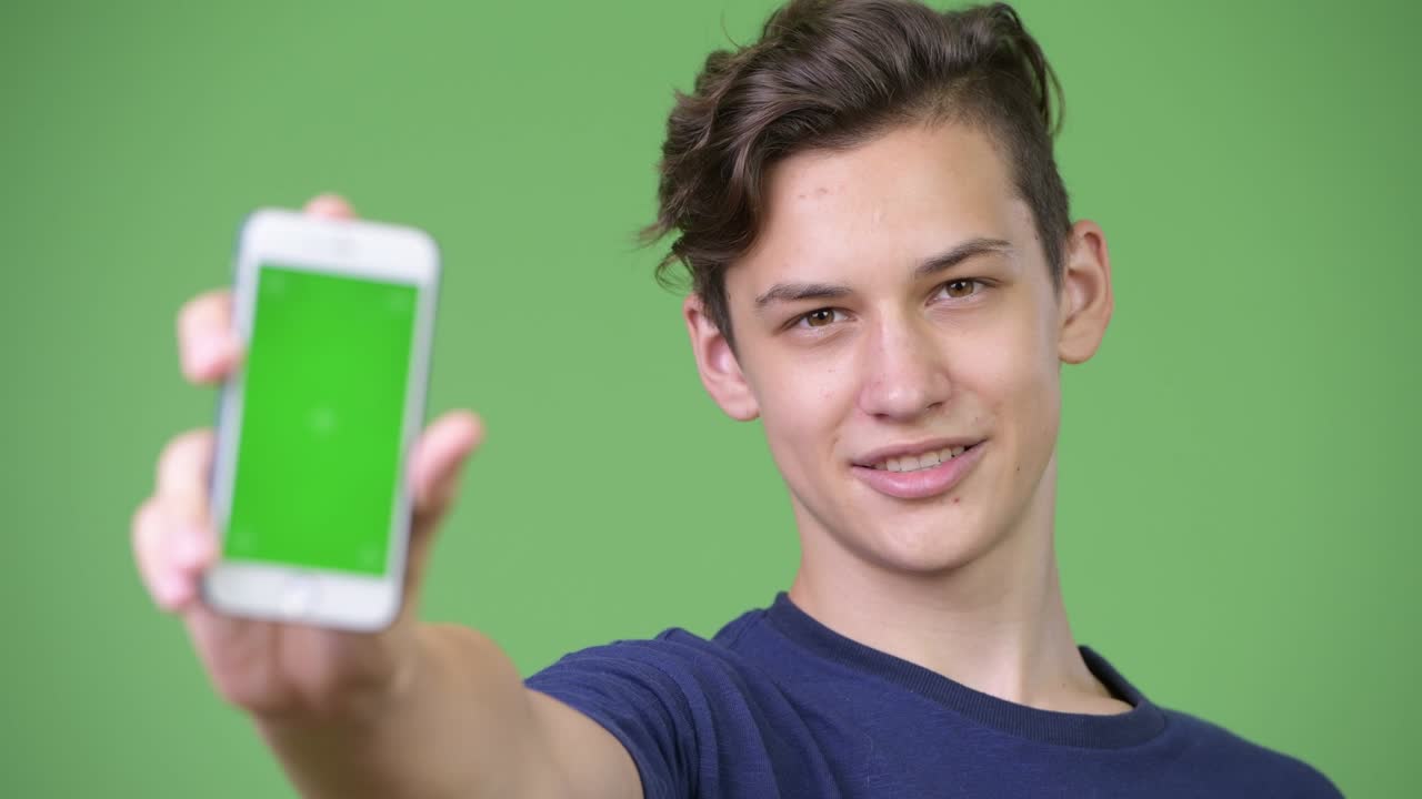 젊은 잘생긴 십대 소년이 전화를 보여줍니다.