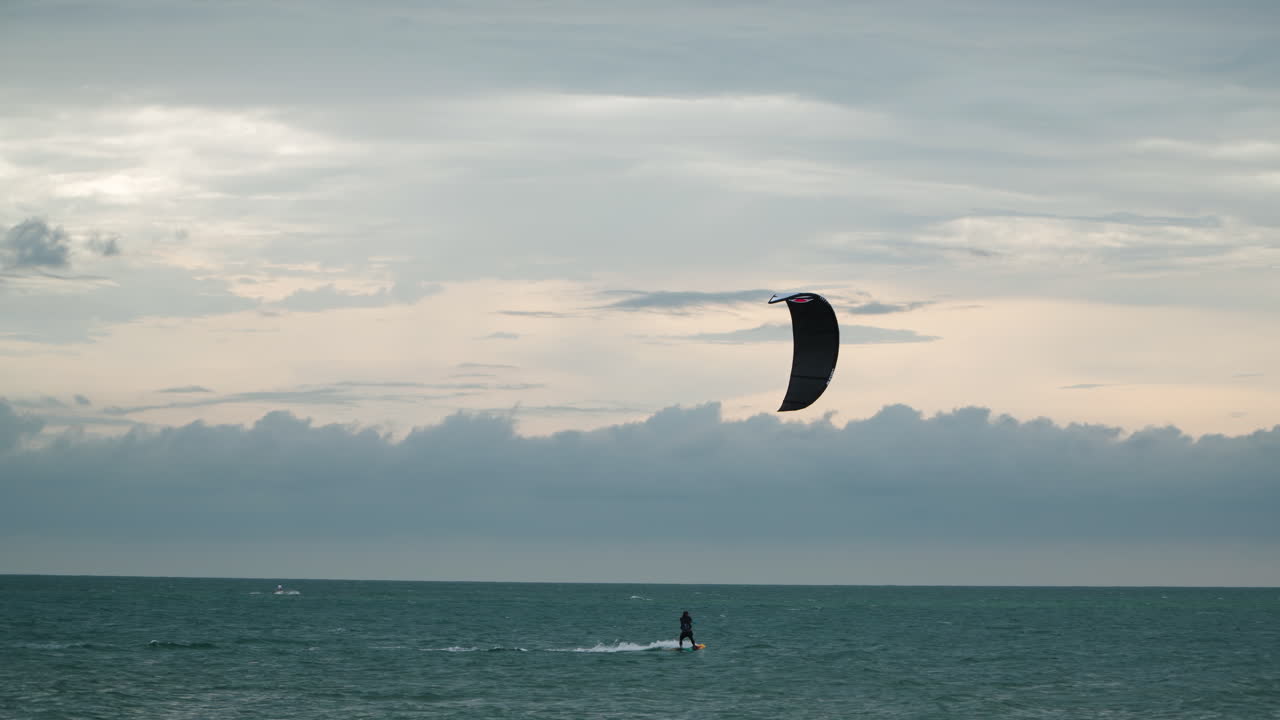 hombre haciendo kitesurf en el océano contra el cielo rosa púrpura de la puesta de sol - tiro de seguimiento de gran angular