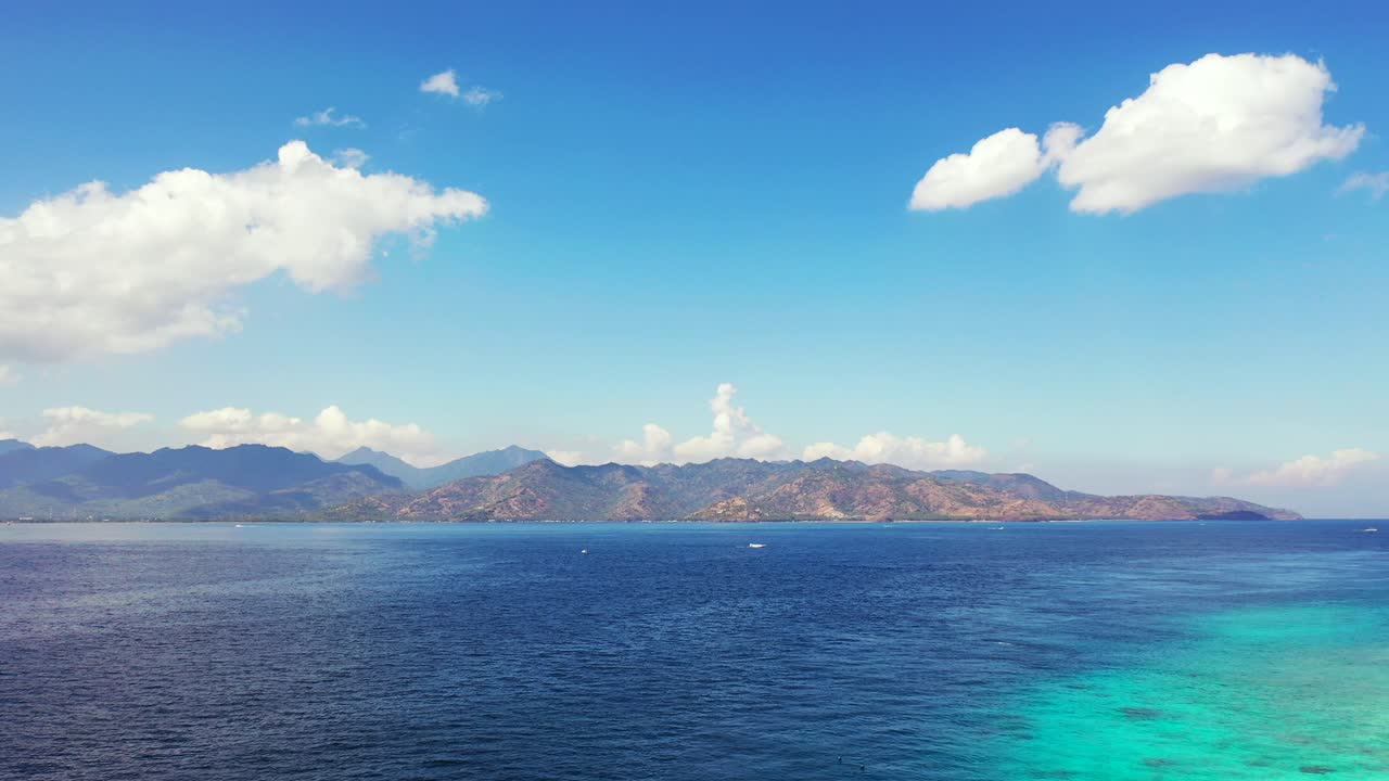 Colorful seascape with blue sea and turquoise lagoon under bright sky with white clouds hanging over mountains of Indonesia