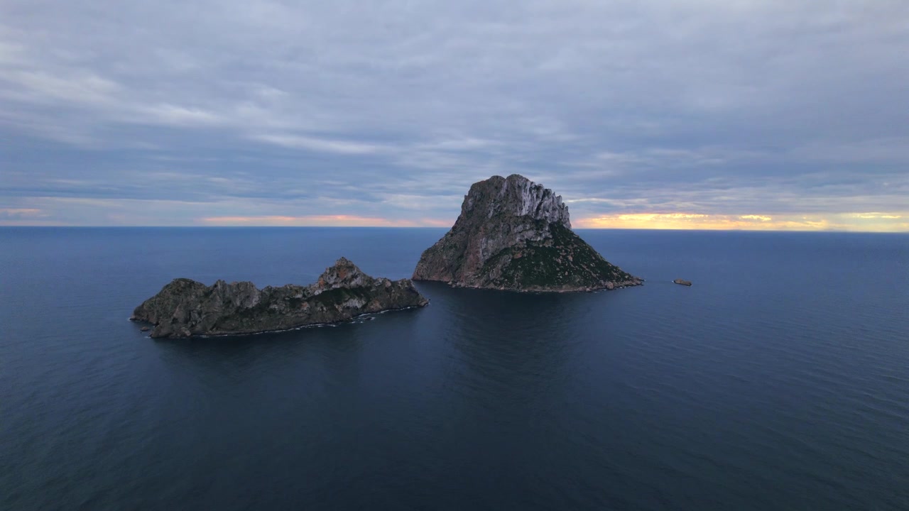 Ripresa aerea in 4K con drone di Es Vedrà al tramonto, Ibiza, Spagna. L'iconica isola rocciosa emerge dal Mar Mediterraneo mentre una calda luce dorata illumina la costa e le acque circostanti