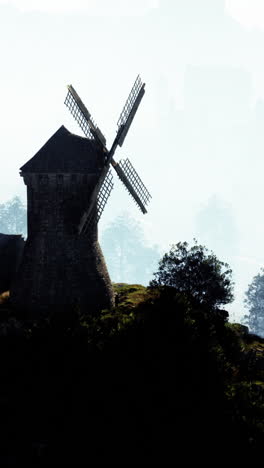 a stone windmill standing tall on a hill with trees and fog in the background