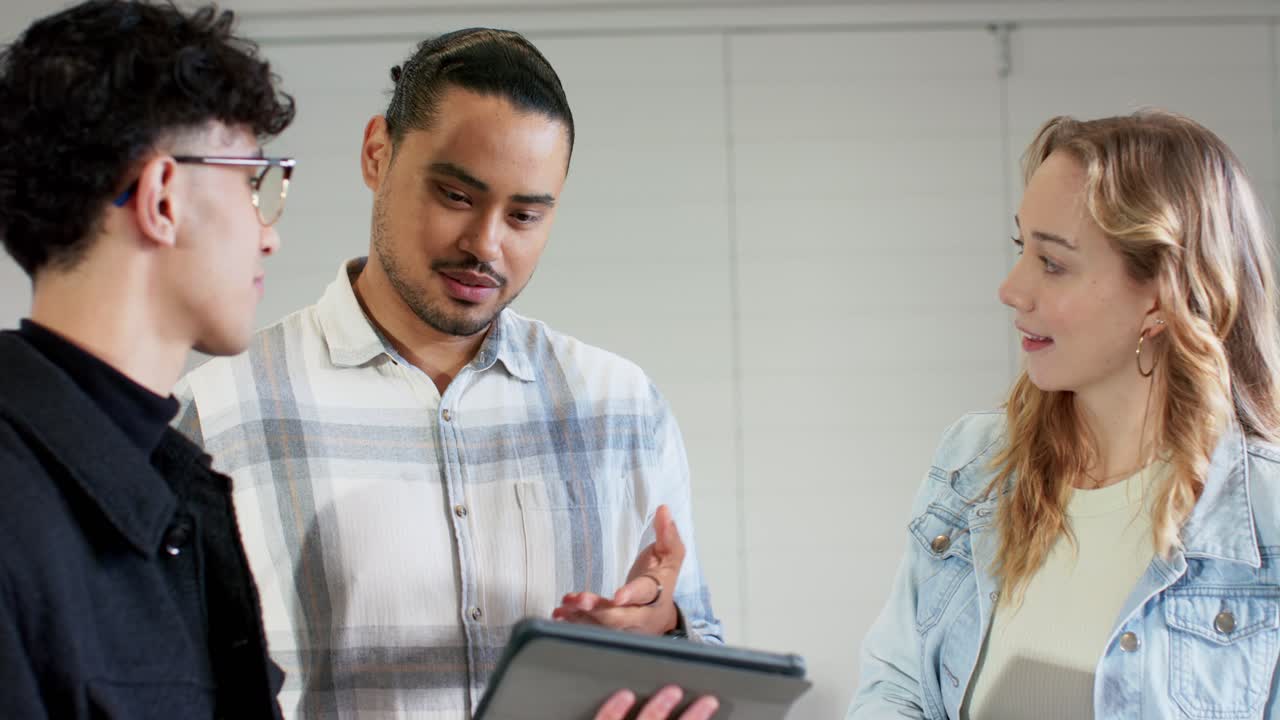 Diverse coworkers tilting tablet to share project update in meeting space while discussing detail