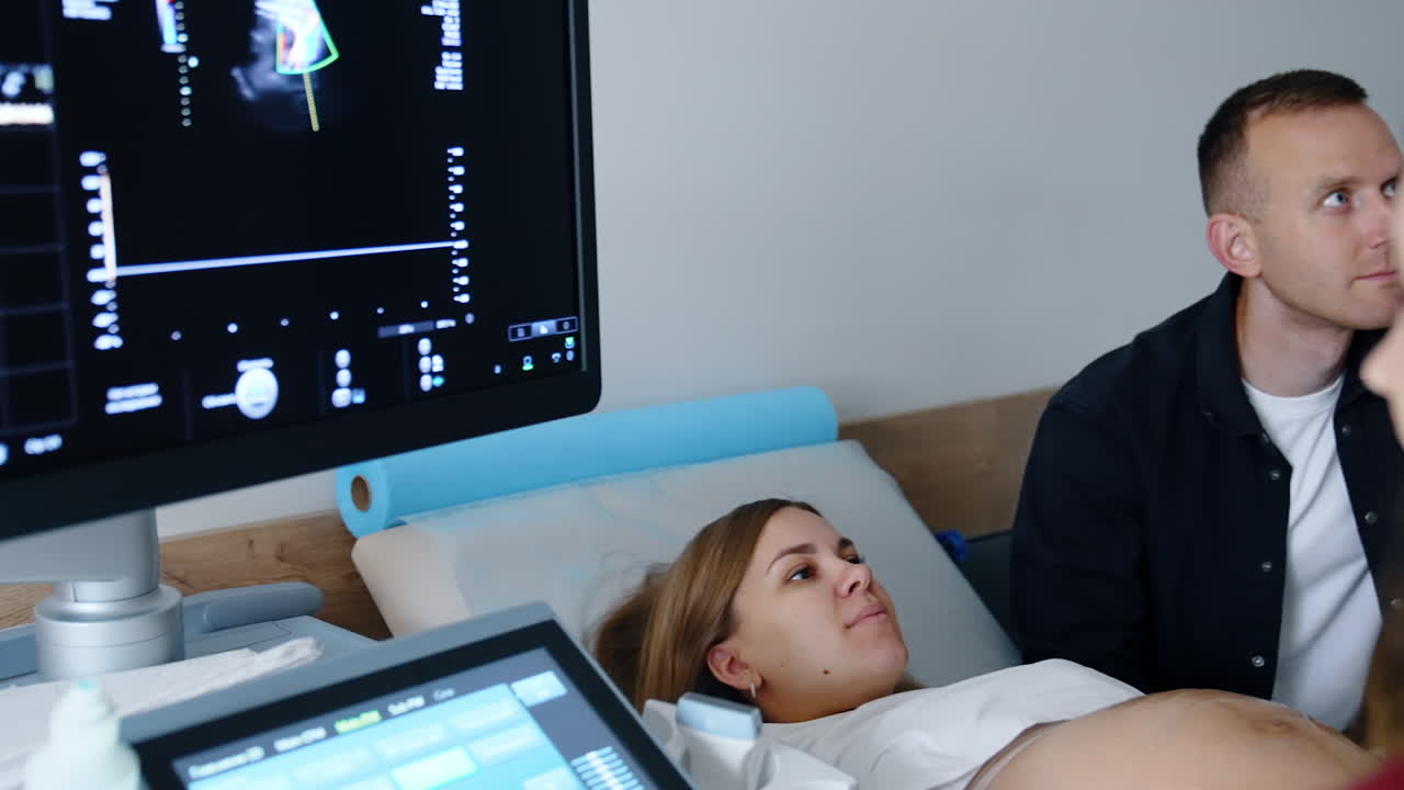 Ultrasonic equipment monitor showing the parameters of a baby in womb. Future parents watch attentively on the screen.