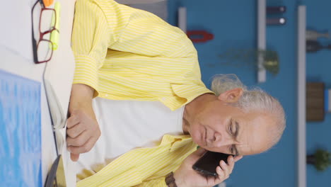 Vertical-video-of-Home-office-worker-old-man-phone-angry-performs-business-call.