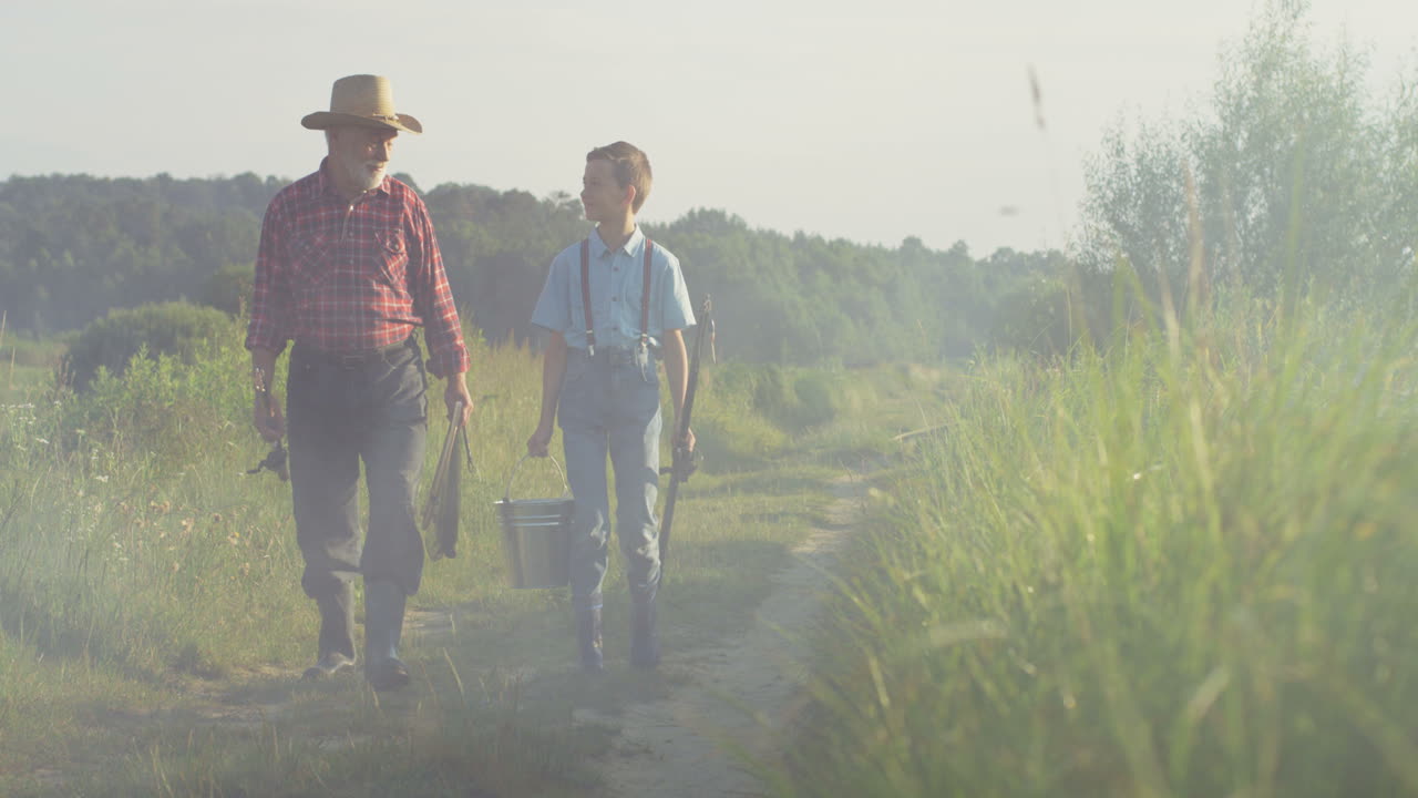 아침에 낚싯대를 들고 백인 할아버지와 그의 어린 손자가 함께 걷는다