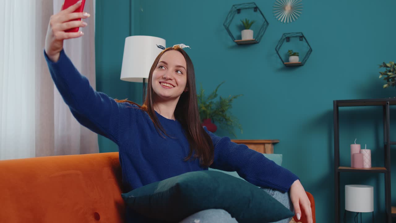 Donna sul divano a casa con lo smartphone che si fa un selfie con la telecamera del telefono cellulare chiamata video virtuale online
