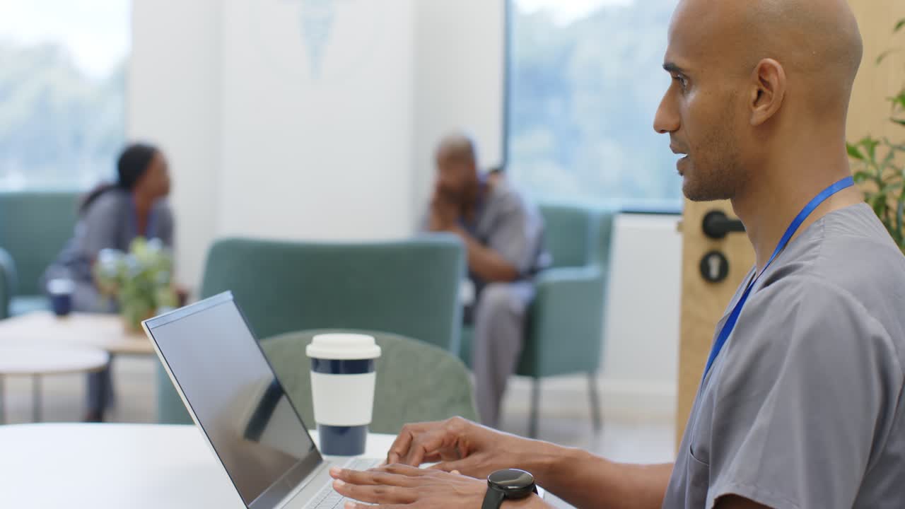 African American staff, man in grey scrubs placing hands on laptop keys, typing, replying in clinic