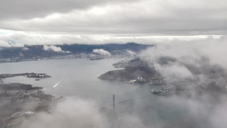 final approach before landing in bergen, norway, shot from airplane with view of downtown bergen between the clouds