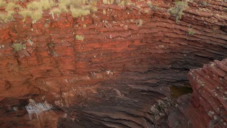 aerial backwards flight showing woman sitting on cliffs during sunset at joffre gorge in karijini national park - cinematic drone shot