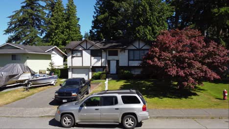 A-stunning-white-detached-house-in-Brookswood,-Langley,-BC-Canada-with-a-lush-garden-of-trees-and-grass-visible-from-the-reverse-aerial-drone-shot