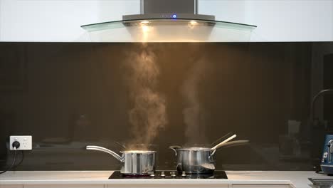 wide shot of a pair of simmering pans on a cook top with steam rising into a rangehood