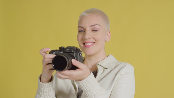 Female caucasian model posing with DSLR against yellow backdrop 01