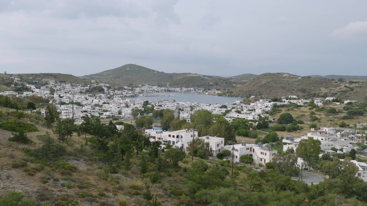 Bir yamaçtan, adanın engebeli arazisine serpiştirilmiş badanalı binalarla Patmos'un Skala koyuna doğru manzara.