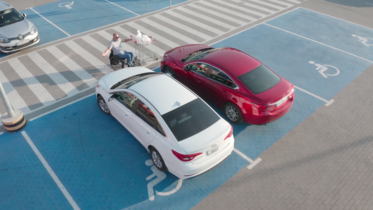 체어 에 앉은 장애인 이 슈퍼마켓 주차장 에서 자기 앞 에 바구니 를 밀고 있다